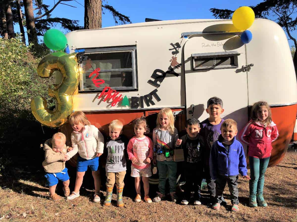 Group photo of kids in front of vintage camper