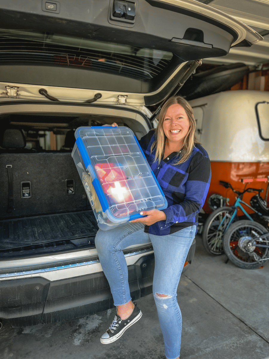 Woman holding a bin of supplies at back of car